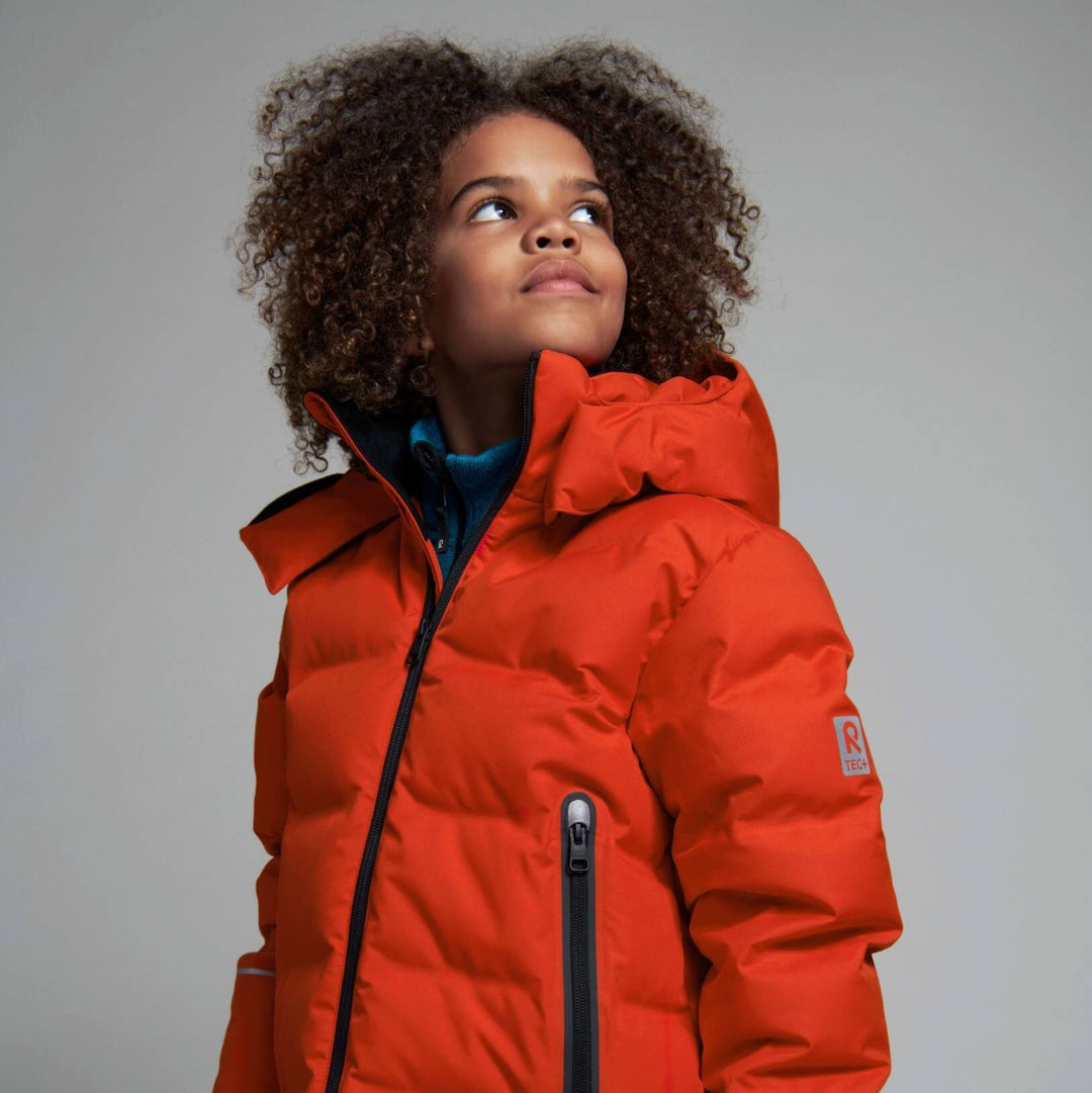 teenager in colourful snow gear wearing a ski helmet and goggles carrying skis