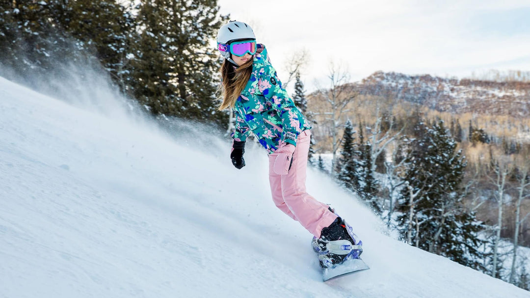 teenager in colourful snow gear wearing a ski helmet and goggles carrying skis