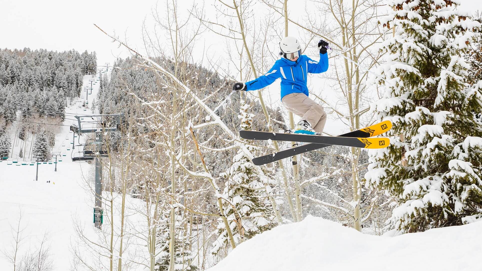 teenager in colourful snow gear wearing a ski helmet and goggles carrying skis
